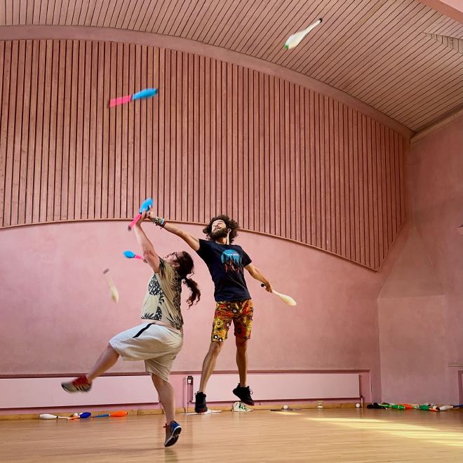 Two jugglers leap in the air, fighting for clubs