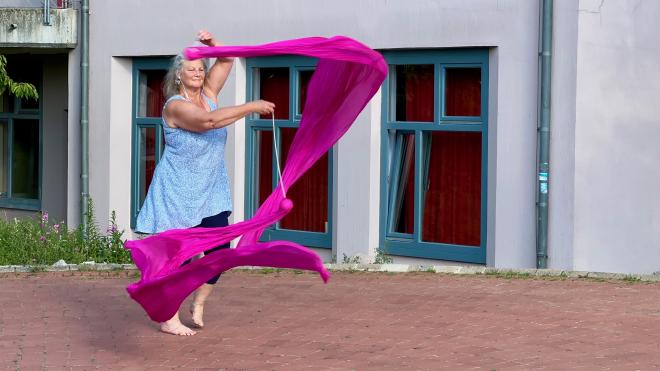 A woman swinging poi with long silk scarves attached