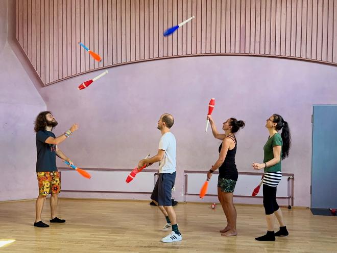 Four jugglers passing clubs in a gym