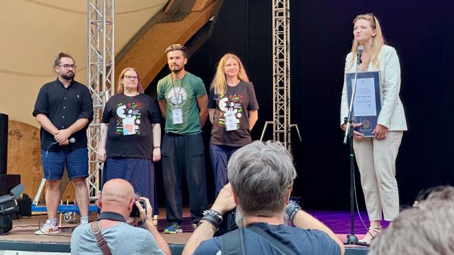 &ldquo;several people on a stage, one presenting a certificate and medallion&rdquo;