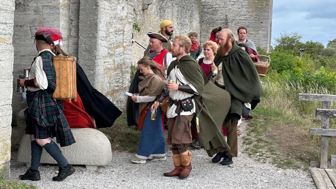 &ldquo;a group of people in medieval dress entering a walled city through a gate&rdquo;