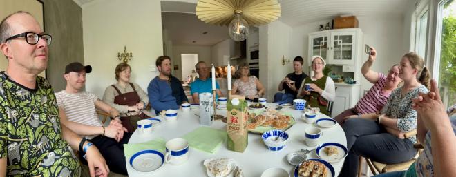 &ldquo;ten people seated around a table with coffee, tea, and sweets&rdquo;