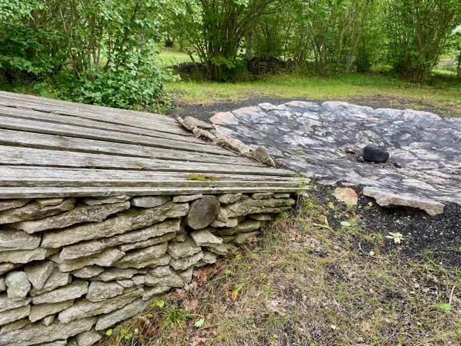 &ldquo;a flat flagstone area with a stone walled, sloping wooden roof structure beside it&rdquo;