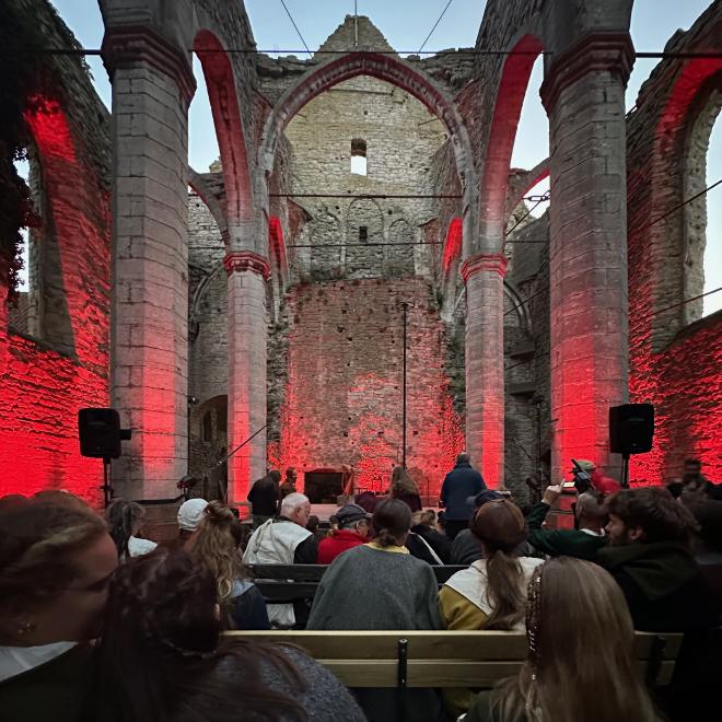 &ldquo;the interior of a ruined church with no roof, set up as a theatre, the stage end illuminated in red&rdquo;