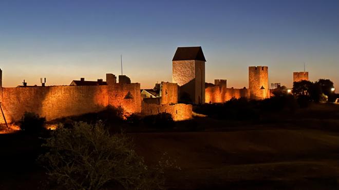 &ldquo;the walls of a medieval city with three towers, illuminated by reddish-orange light&rdquo;