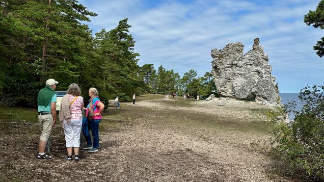 &ldquo;three people clustered around a park sign, with a large rauk in the background&rdquo;