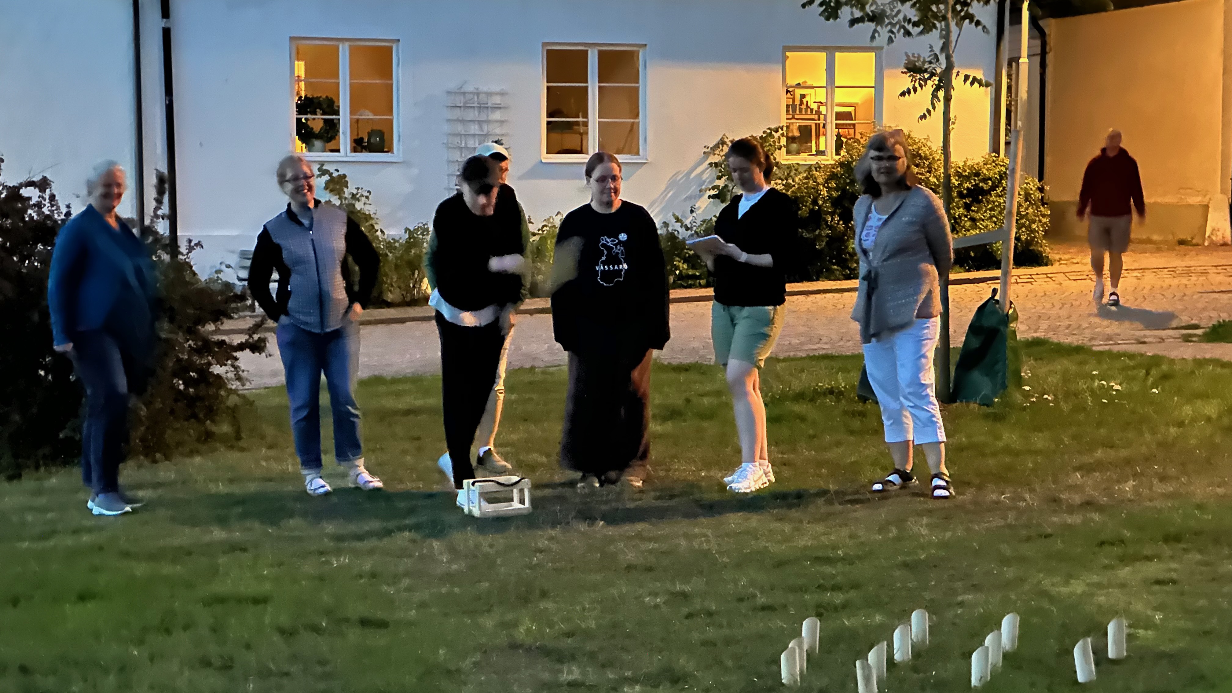 &ldquo;seven people standing on a lawn, a few metres back from some wooden pegs. one person is throwing a wooden dowel at the pegs&rdquo;